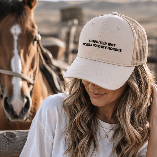 Woman wearing cream western trucker hat embroidered with absolutely not gonna hold my horses at a roadside country stop