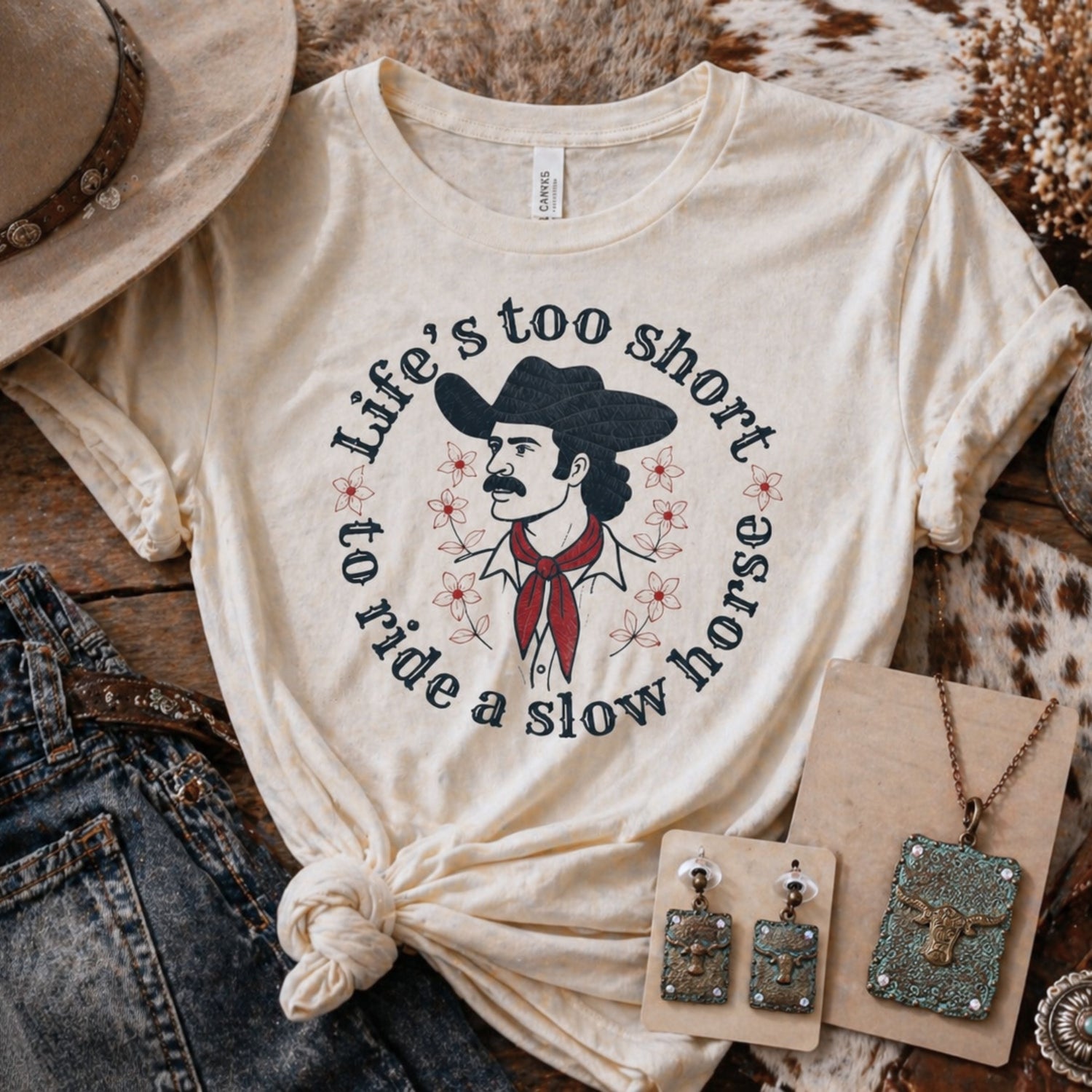 Western clothing outfit with graphic tee, denim jeans, cowboy boots, and turquoise jewelry, rustic vintage western style flat lay