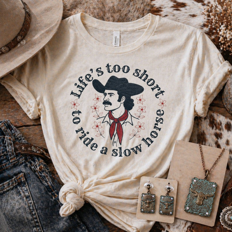 Western clothing outfit with graphic tee, denim jeans, cowboy boots, and turquoise jewelry, rustic vintage western style flat lay