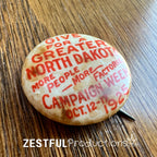 Angled view of 1925 North Dakota “Give for a Greater North Dakota” Campaign Week celluloid button showing patina and original pin.
