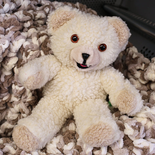 Authentic 1986 Lever Brothers Snuggle mascot plush seated on a cozy neutral blanket. This vintage 10-inch advertising collectible features fluffy ivory sherpa-style fur, amber safety eyes, and a cheerful smile, making it a charming addition to retro toy collections, laundry room decor, or nostalgic home displays.