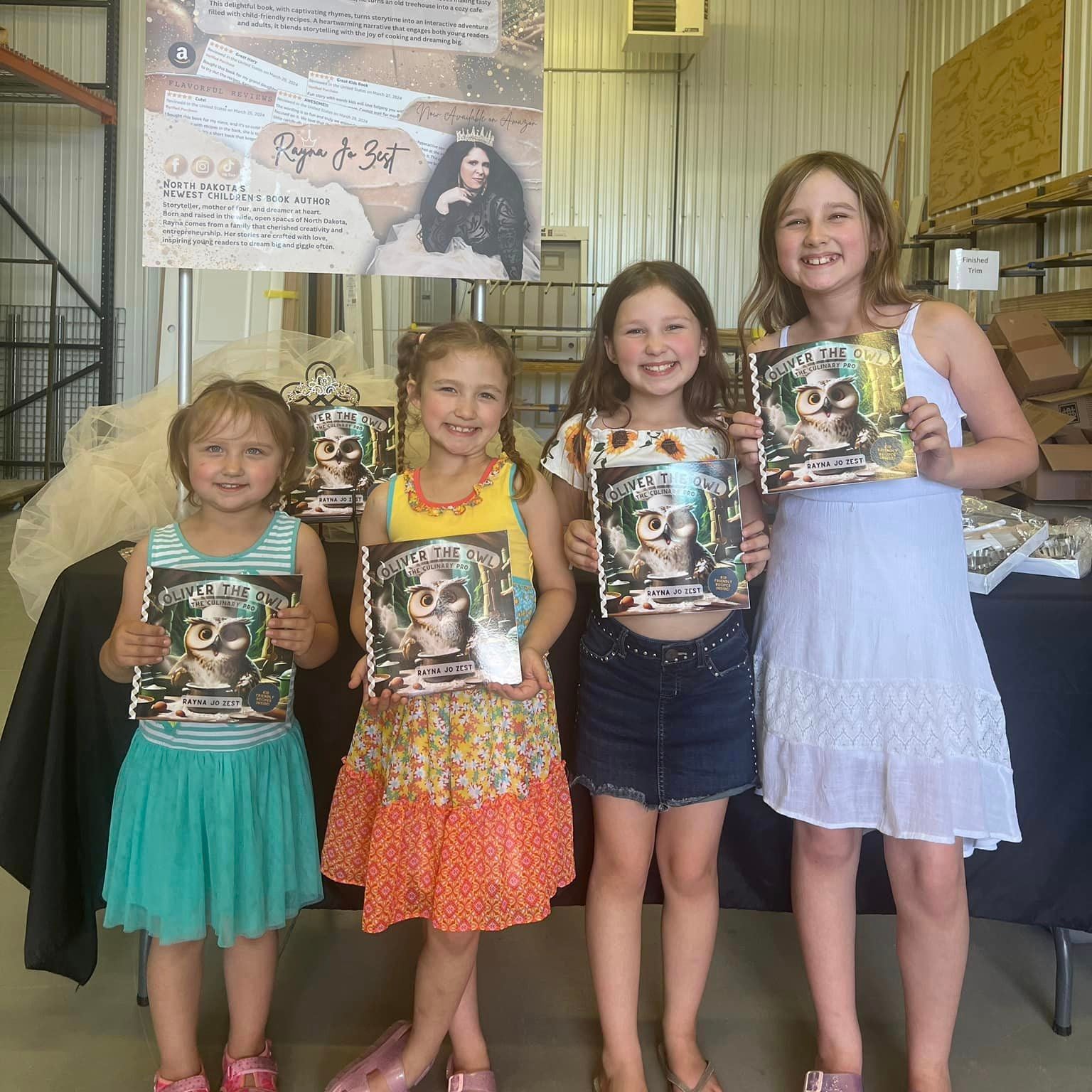 Four young girls holding books in front of a banner with a character on it.