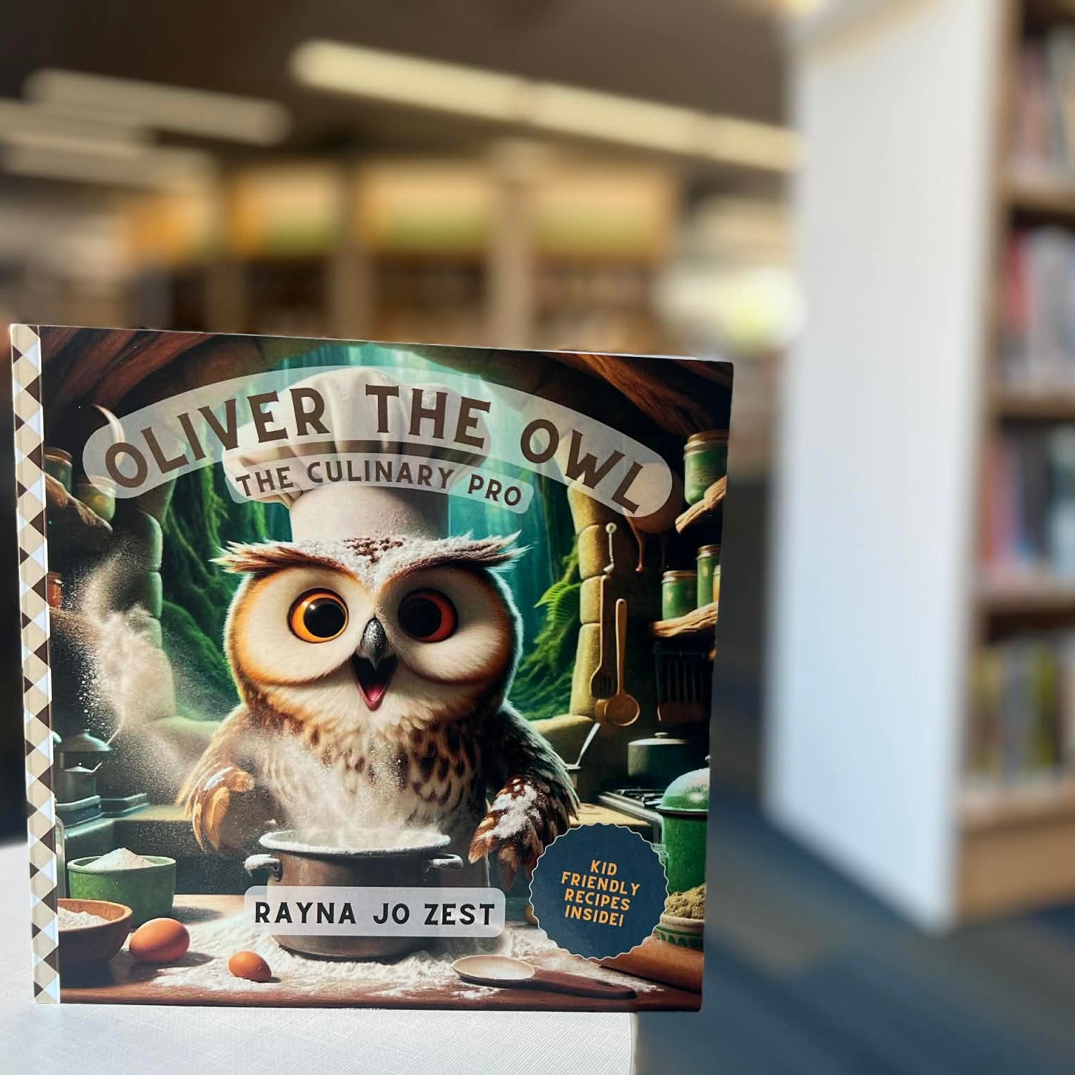 Book titled 'Oliver the Owl: The Culinary Pro' by Rayna Jo Zest in a library setting.