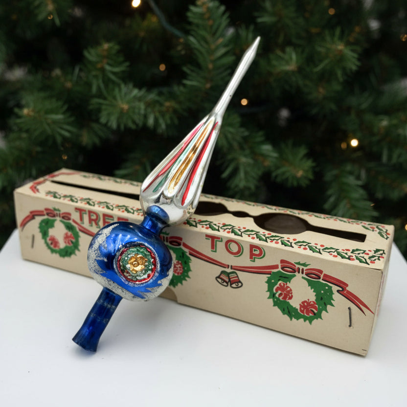Decorative Christmas tree topper with a blue and silver design, placed on a cardboard box with Christmas graphics.