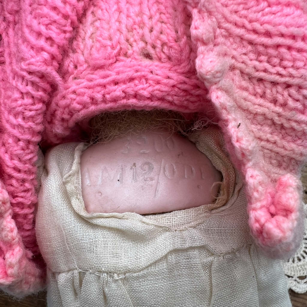 Close-up of the recessed markings on the back of the doll’s head, with the pink knitted clothing lifted and the cream garment visible below.
