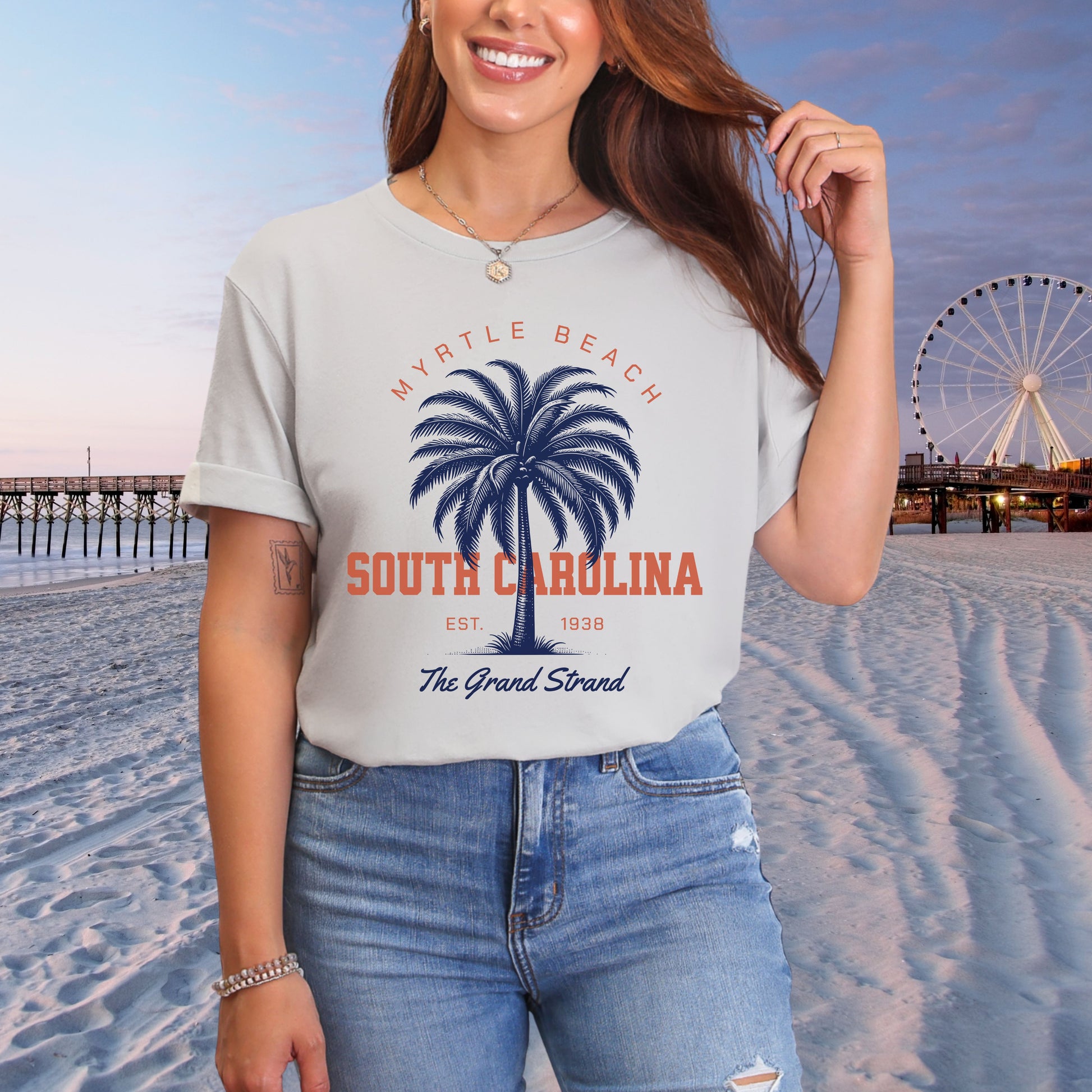 Person wearing a t-shirt with 'Myrtle Beach, South Carolina' design on a beach with a Ferris wheel in the background.