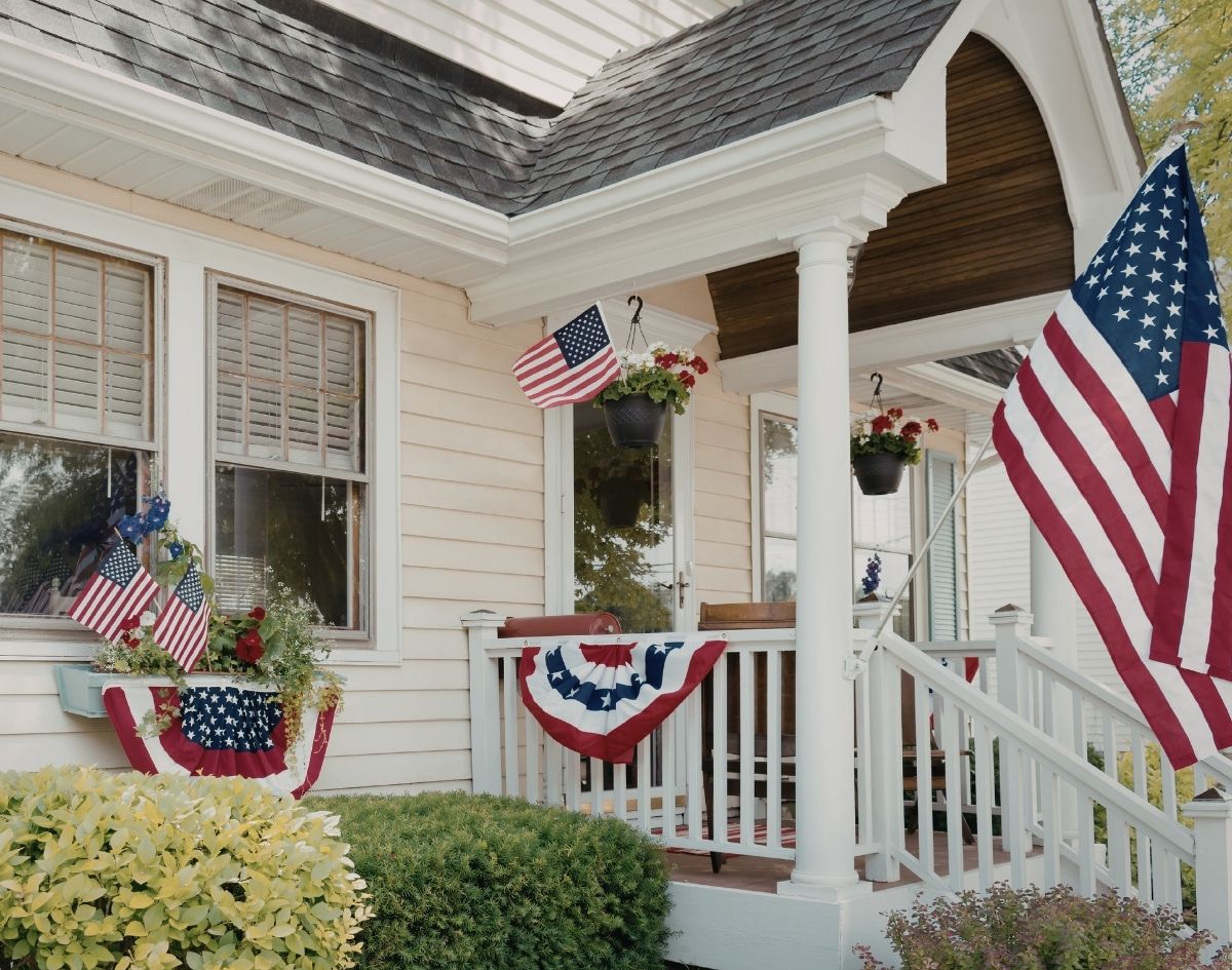 Front porch decorated with American flags and red, white, and blue bunting, showcasing classic patriotic summer home decor and Americana style for an American Summer collection.