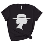 Black crewneck graphic tee with rolled sleeves and a knotted hem, shown flat against a white background. A light-colored silhouette depicts a woman in side profile wearing a wide-brimmed hat.