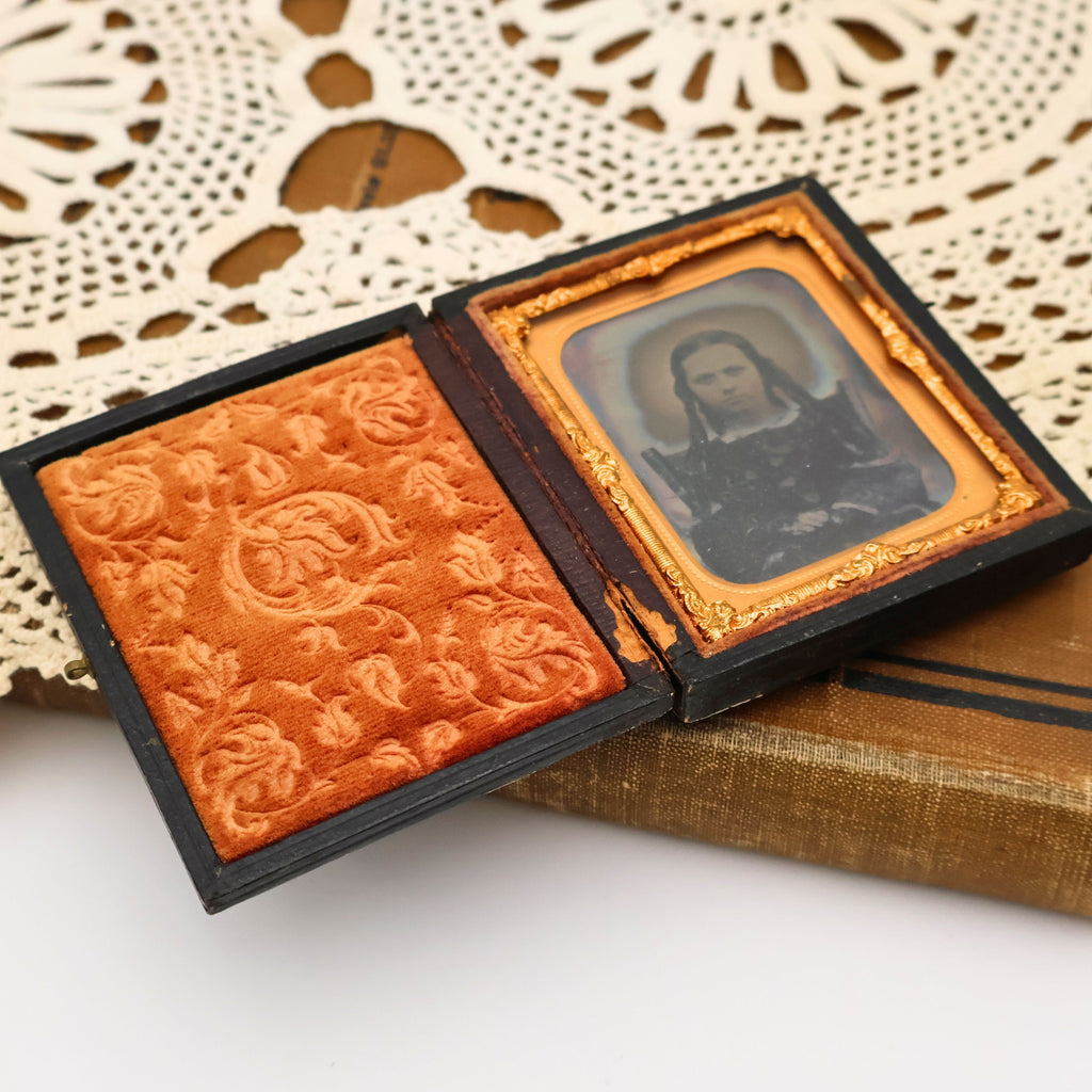 Open display of the antique ambrotype portrait showing the embossed velvet interior opposite the original gilt brass mat surrounding the glass image. This nineteenth-century photograph is presented exactly as photographed with authentic antique character and age.