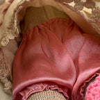 Close-up beneath the cream dress showing the doll’s pink underclothing, gathered waistband, fabric folds, and surrounding skirt trim.