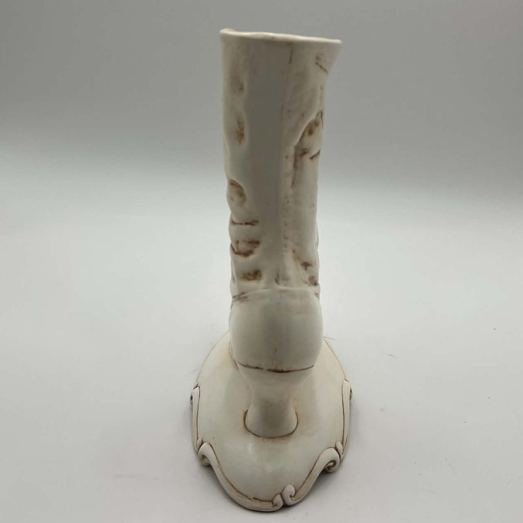 Rear view of a tall vintage Victorian boot vase showing the smooth back of the ceramic shaft, sculpted folds and small heel rising above an ornate pedestal base. Visible finish variations and brown distressed accents contribute to its hand-decorated vintage character.