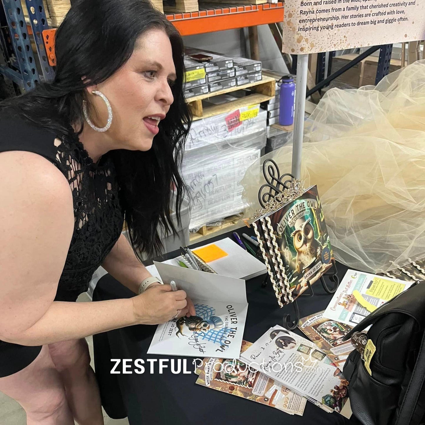 author Rayna Jo Zest signing Oliver the Owl children’s cookbook storybook at book event table with promotional materials