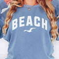 Blue jean beach crewneck sweatshirt close up on woman, oversized fleece pullover with beach graphic, soft fabric texture and relaxed coastal outfit detail