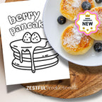 berry pancake coloring page from kids activity book next to real mini pancakes with blueberries on plate for cooking and learning fun
