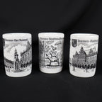 Front view of three coordinating white porcelain Bremen souvenir shot glasses displayed in a row. Black illustrations show the Roland statue beside historic buildings, the stacked Bremen Town Musicians, and the ornate Rathaus, with German titles above each scene.