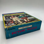 Angled view of the original Built-Rite picture puzzle box showing the Ours to Protect title label and No. 300 on the side. The lid depicts children beside a red bicycle, with blue packaging, pink lettering, yellow accents, and worn corners and edges.