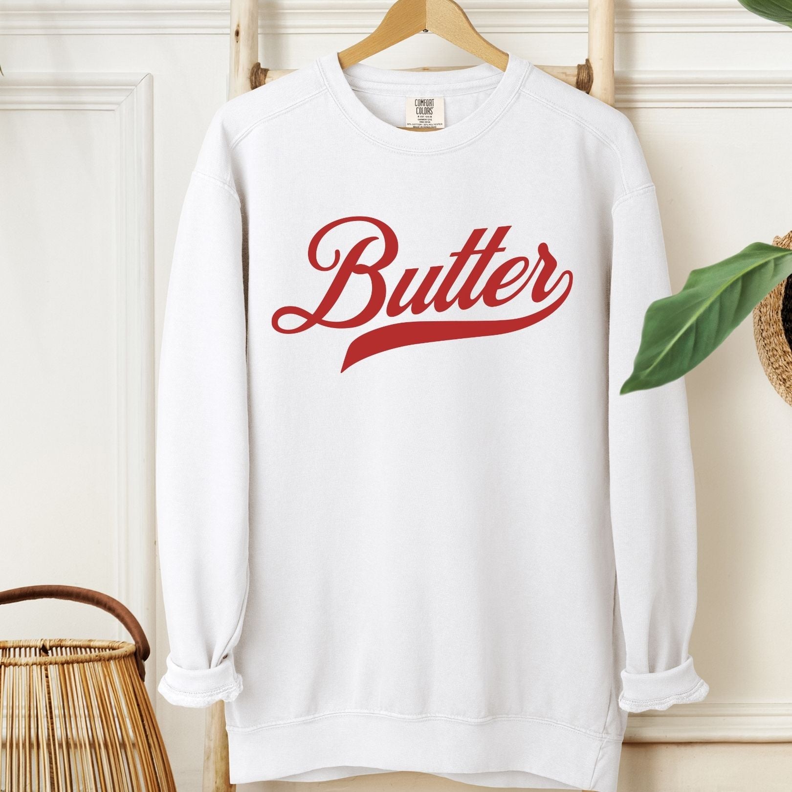 Butter script crewneck sweatshirt displayed on hanger in neutral setting. Vintage inspired graphic sweatshirt with bold lettering. Stylish and comfortable pullover for casual everyday outfits.