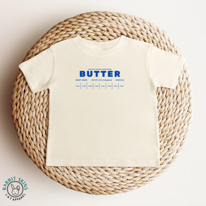 Natural color butter infant tee with bold blue lettering in flat lay. Neutral baby outfit piece with simple playful design.