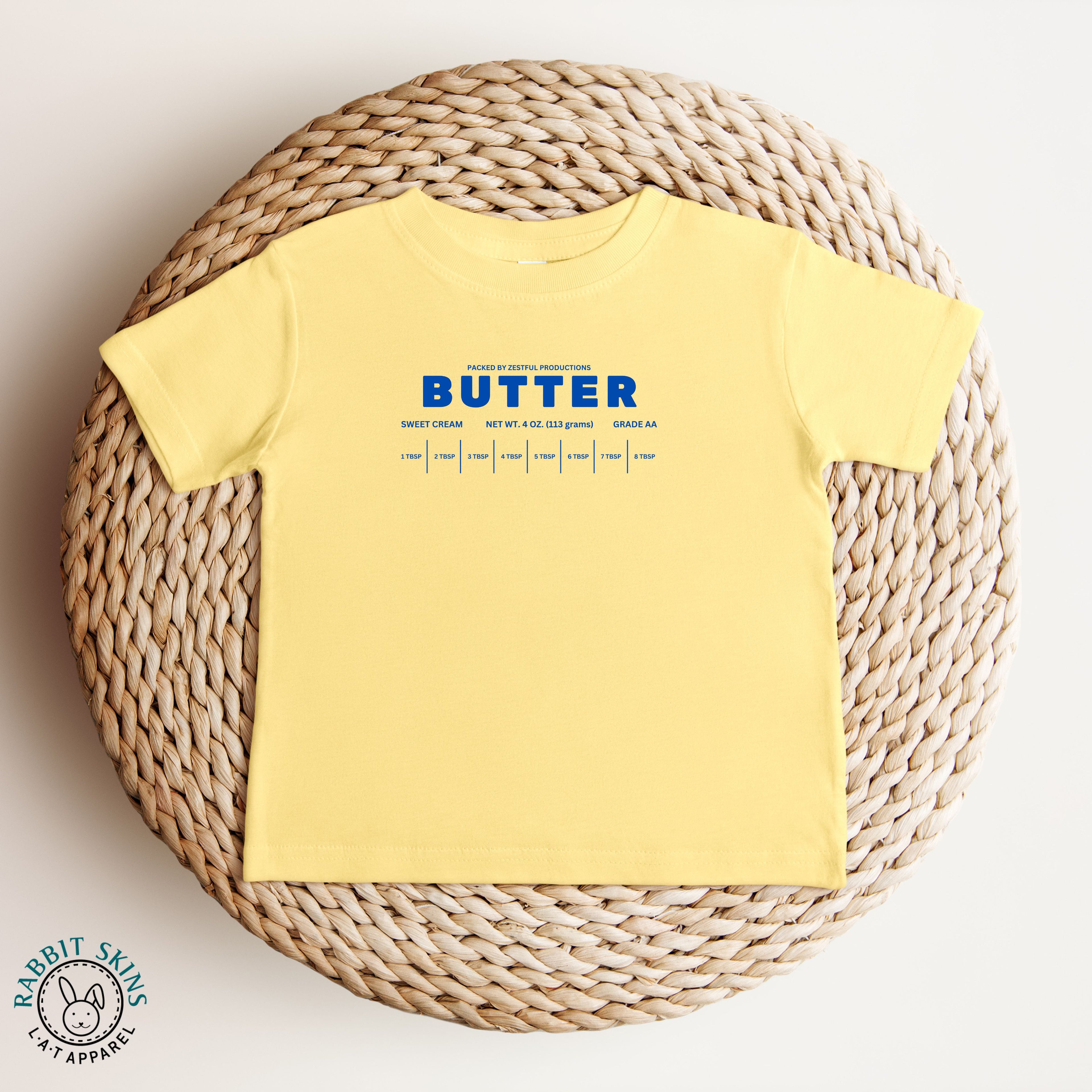 Yellow butter infant tee displayed in flat lay with bold blue lettering. Soft baby shirt for comfortable everyday outfits and playful styling.