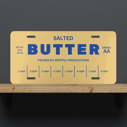 Butter license plate displayed on shelf with bold butter stick design and blue lettering. Funny novelty decor piece for kitchens, offices, or gift giving.