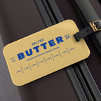 Butter luggage tag attached to suitcase with bold butter stick design and blue lettering. Funny travel accessory that makes bags easy to spot and adds personality to luggage.