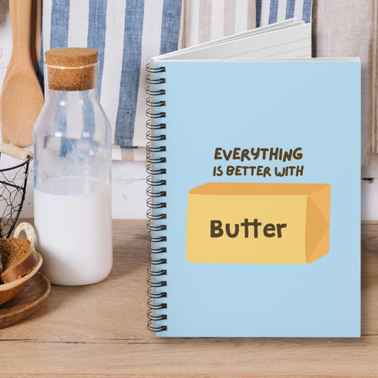 Butter notebook with blue cover and butter graphic displayed on kitchen counter. Spiral journal for notes, lists, and everyday writing with playful design.