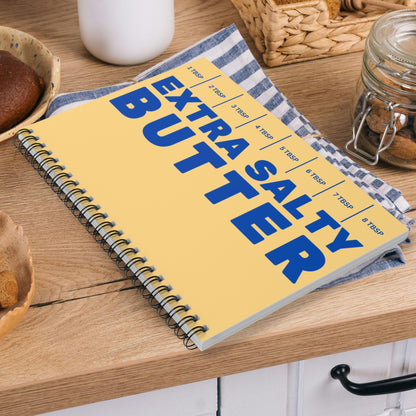 Butter notebook with bold yellow and blue design placed on kitchen counter. Spiral journal perfect for notes, lists, and everyday use with playful personality.
