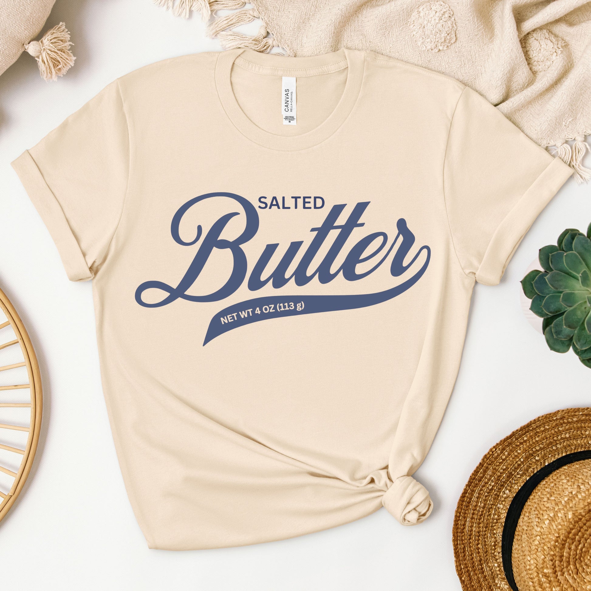 Neutral toned butter script graphic tee displayed in flat lay. Soft cotton shirt with bold lettering design perfect for layering and everyday casual style.