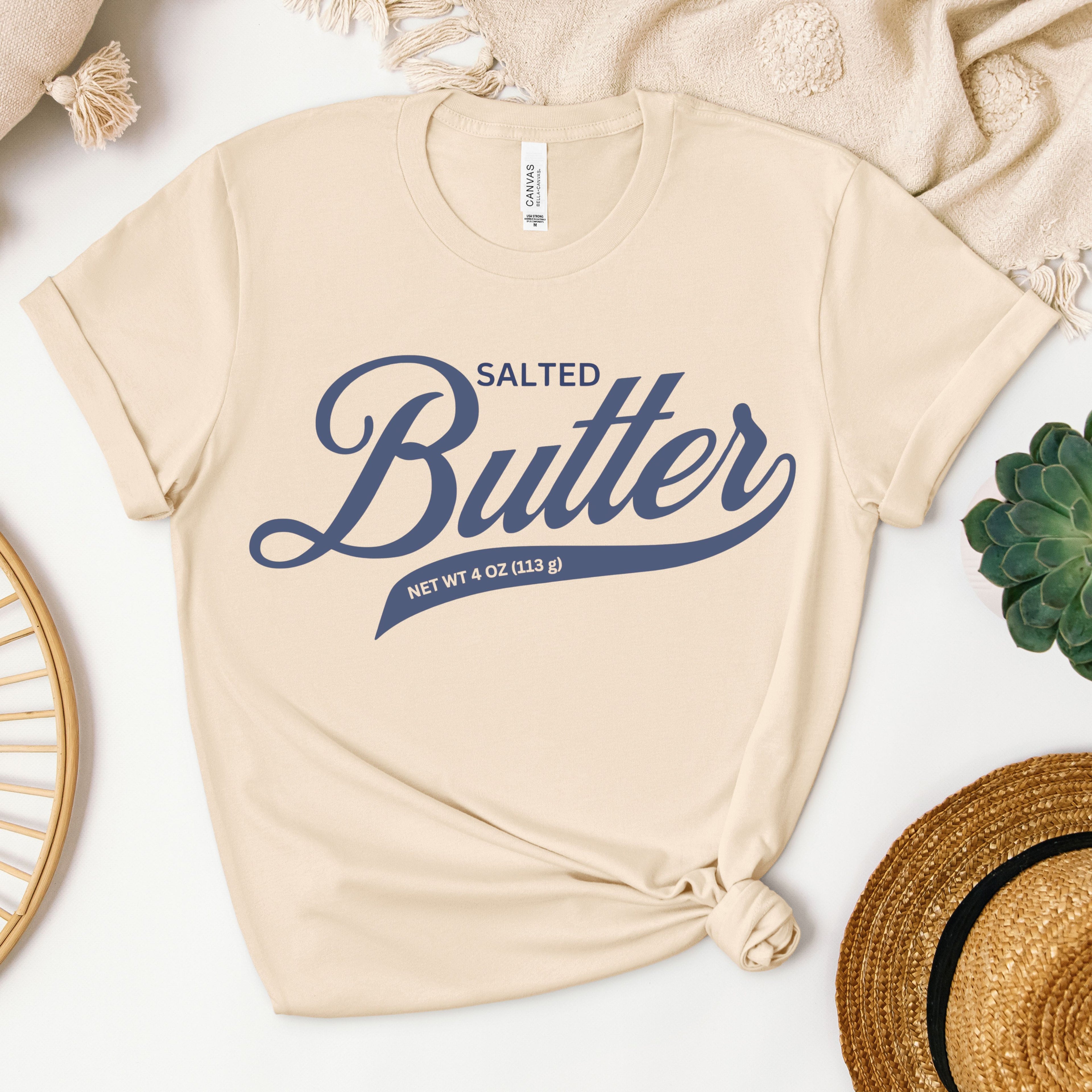 Neutral toned butter script graphic tee displayed in flat lay. Soft cotton shirt with bold lettering design perfect for layering and everyday casual style.