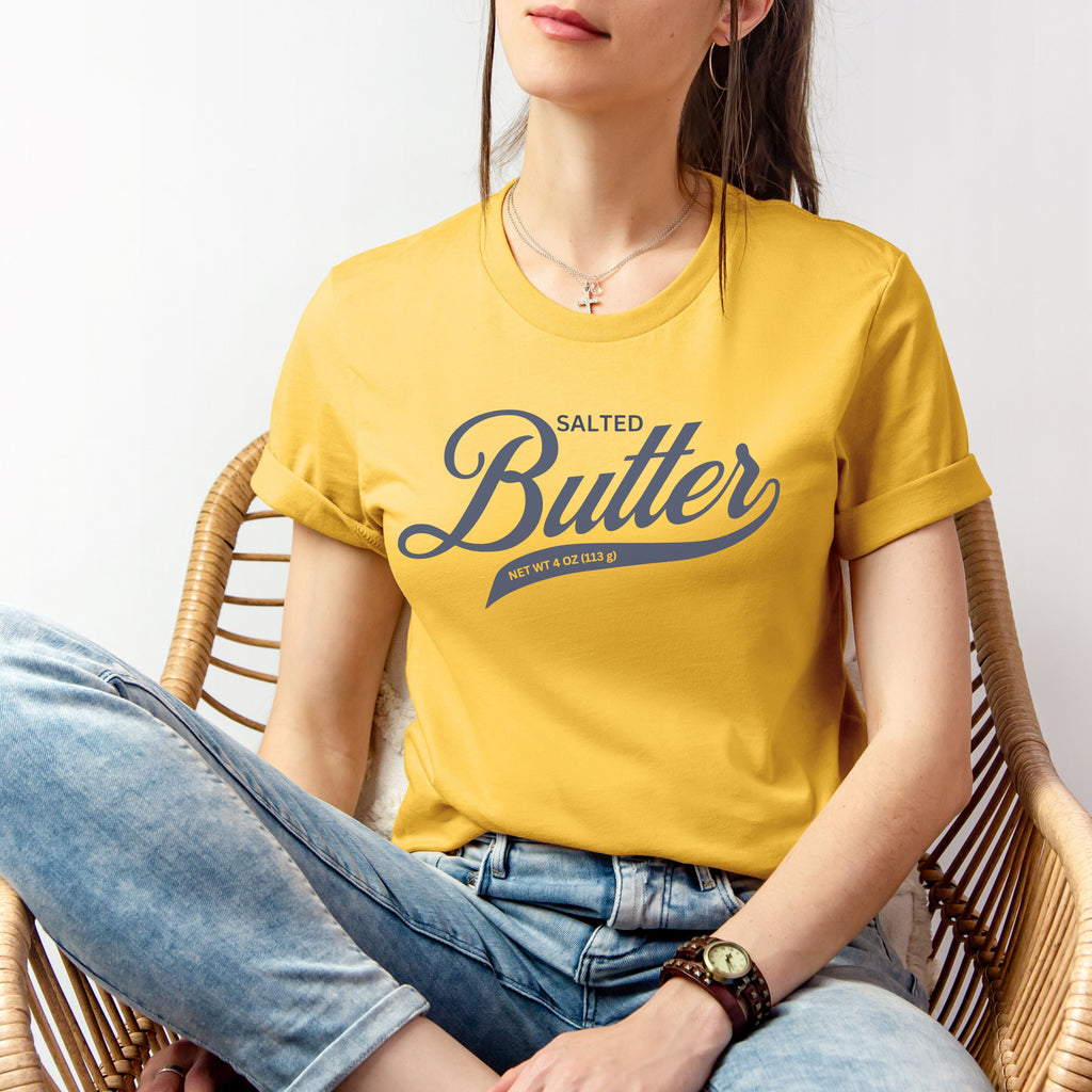 Yellow butter script shirt worn in relaxed seated pose. Soft cotton graphic tee with bold lettering perfect for casual outfits and laid back style.