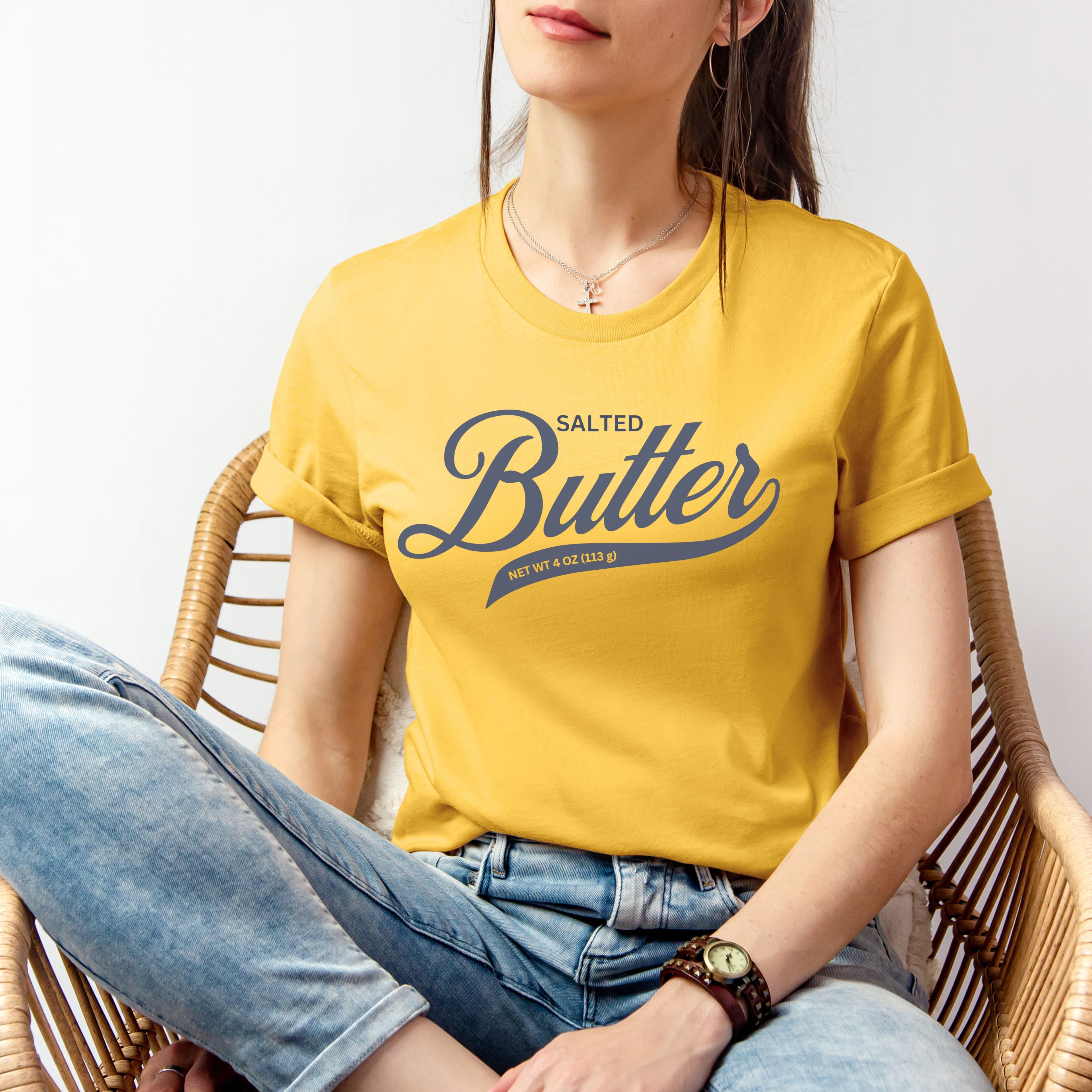 Yellow butter script shirt worn in relaxed seated pose. Soft cotton graphic tee with bold lettering perfect for casual outfits and laid back style.
