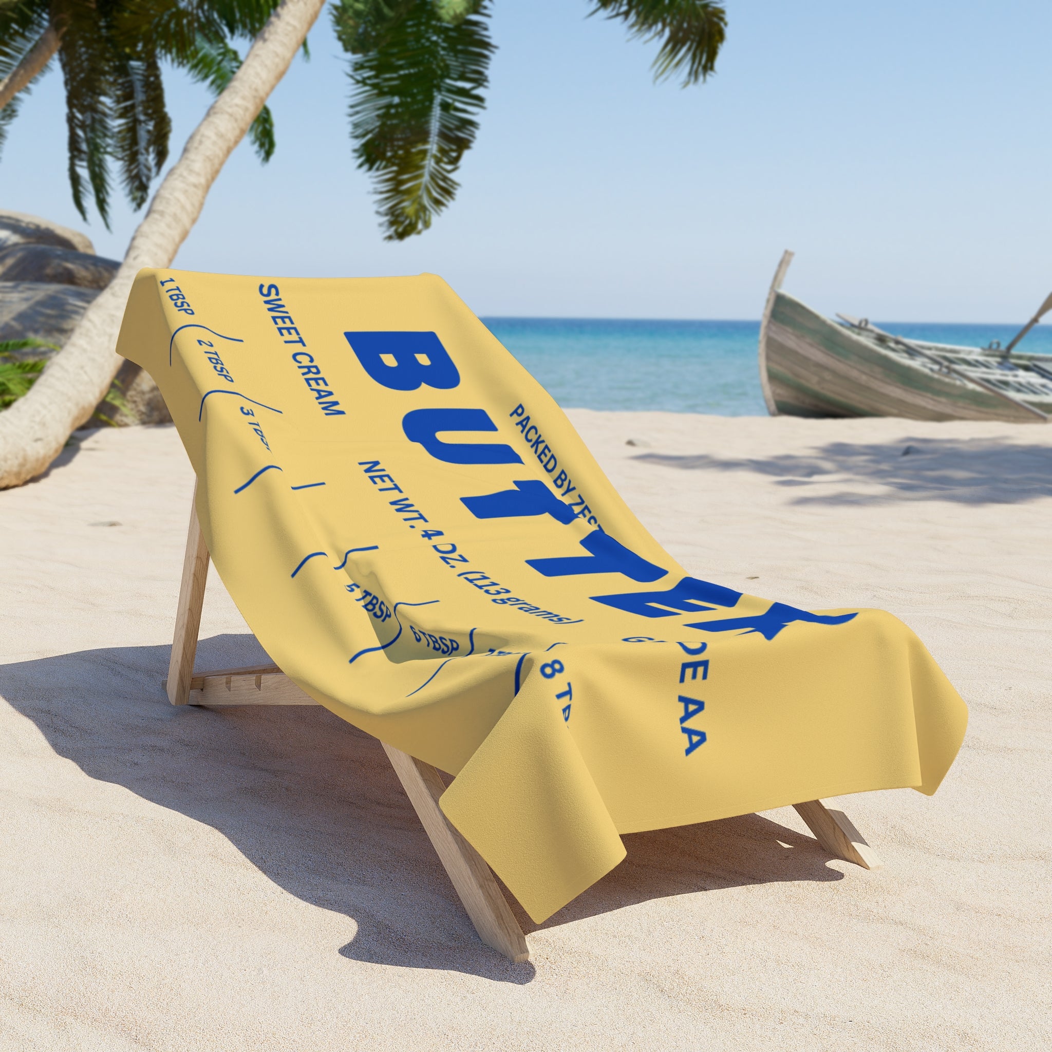 Butter themed beach towel draped over lounge chair by the ocean. Playful summer accessory with bold graphic design, ideal for poolside relaxation and beach day style.