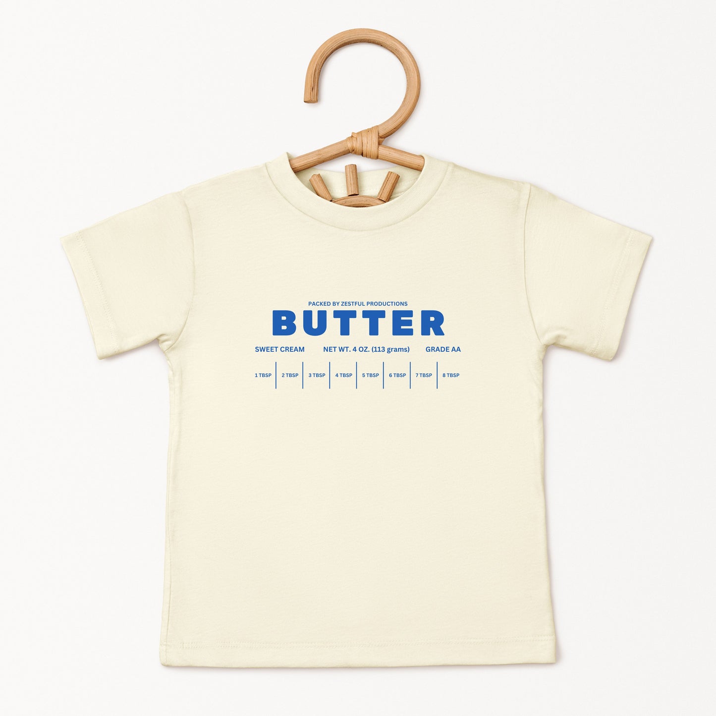 Cream butter toddler tee displayed on hanger featuring retro sweet cream baking graphic and boutique foodie style. Trendy preschool apparel designed for birthdays, playful outfits, and aesthetic kids fashion.