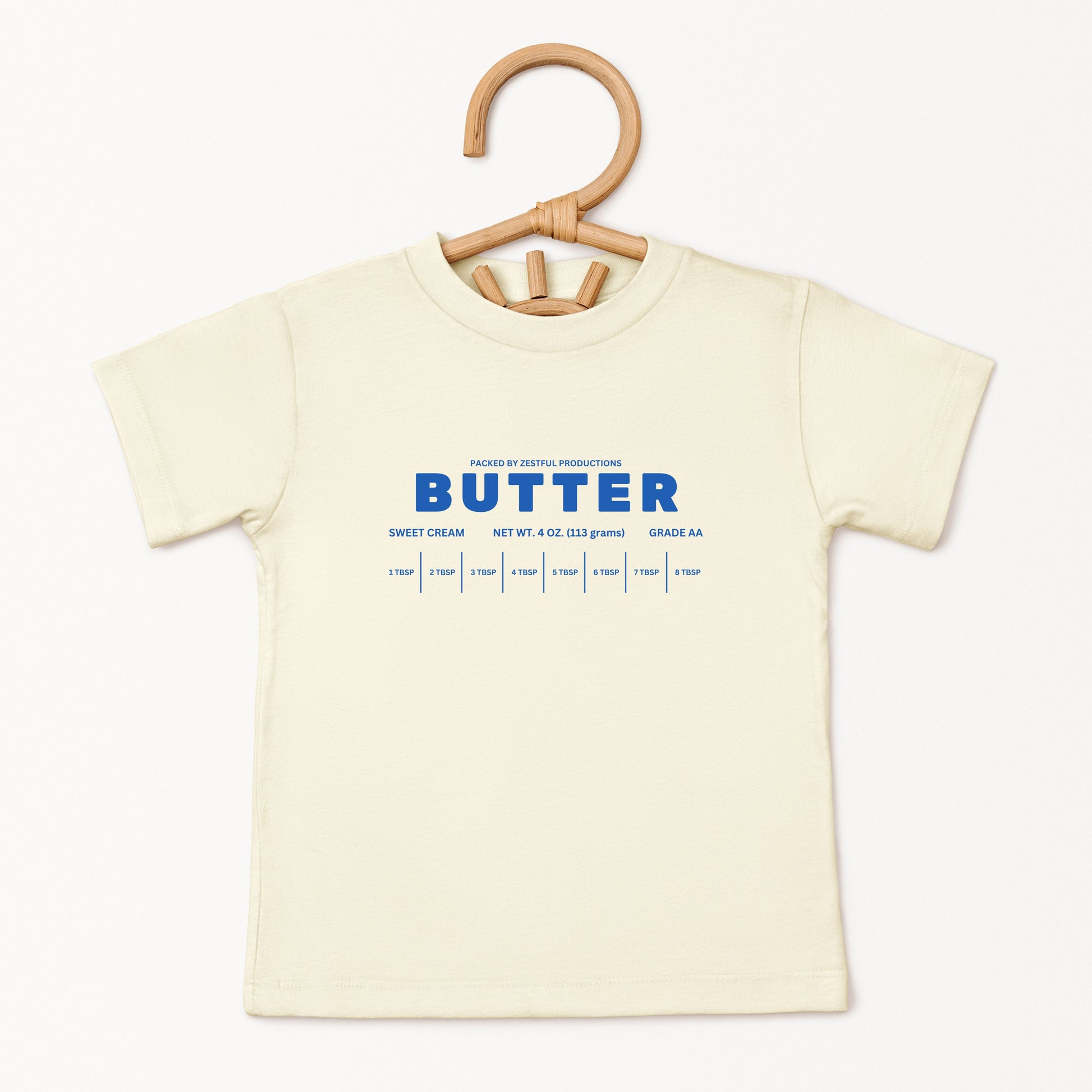 Cream butter toddler tee displayed on hanger featuring retro sweet cream baking graphic and boutique foodie style. Trendy preschool apparel designed for birthdays, playful outfits, and aesthetic kids fashion.