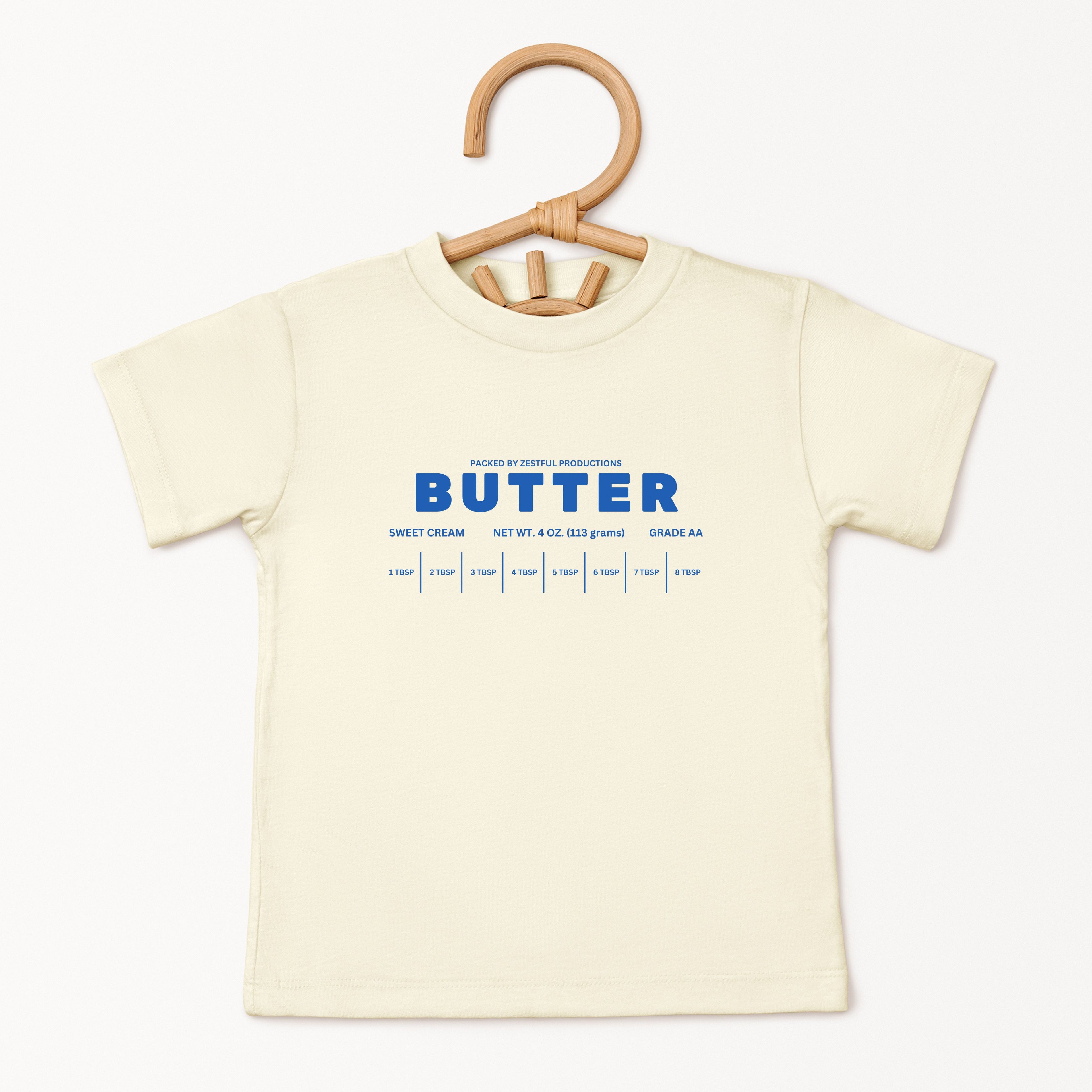 Cream butter toddler tee displayed on hanger featuring retro sweet cream baking graphic and boutique foodie style. Trendy preschool apparel designed for birthdays, playful outfits, and aesthetic kids fashion.