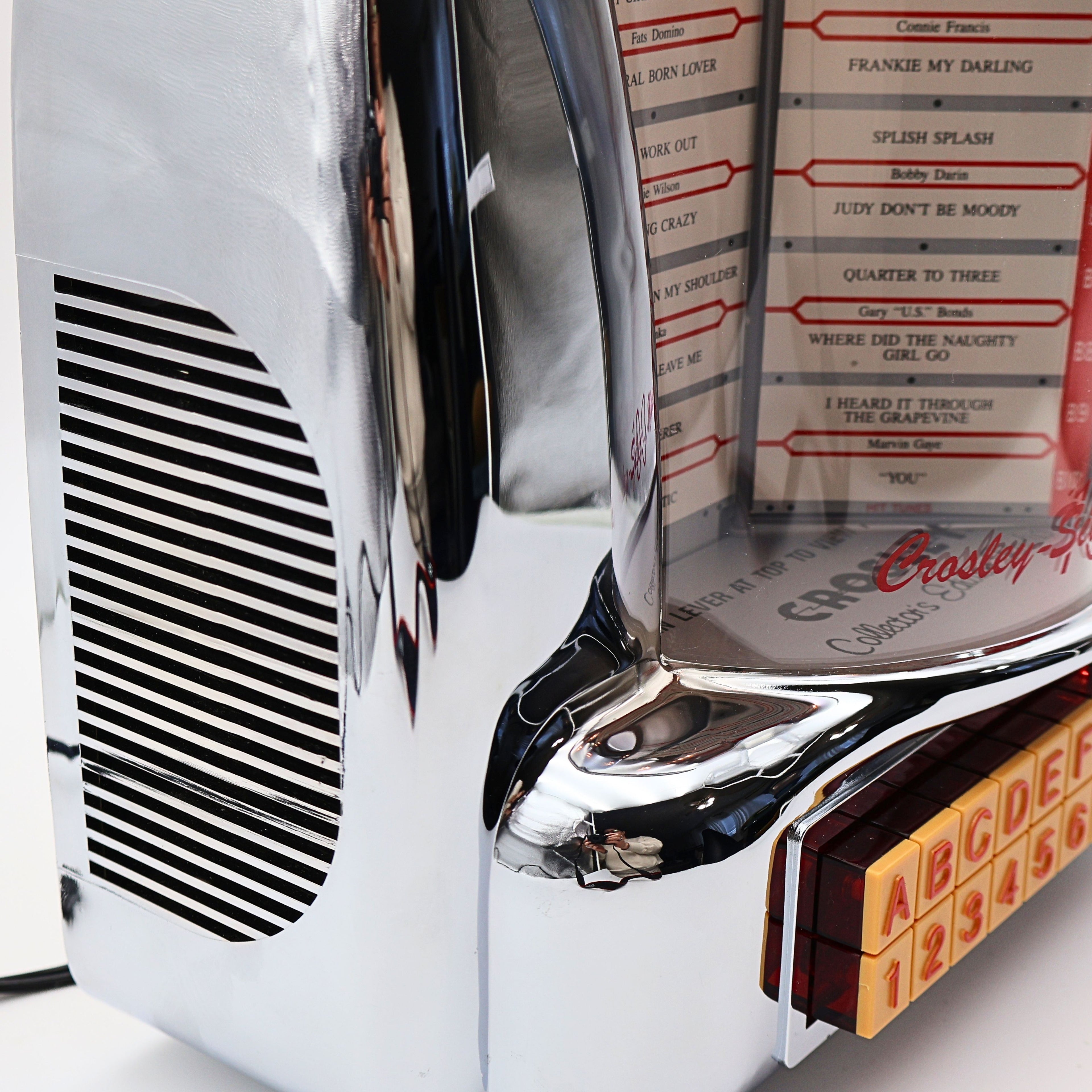 Side view detail of Crosley CR-9 jukebox radio chrome speaker grille and curved housing, retro 1950s diner inspired design with polished reflective finish