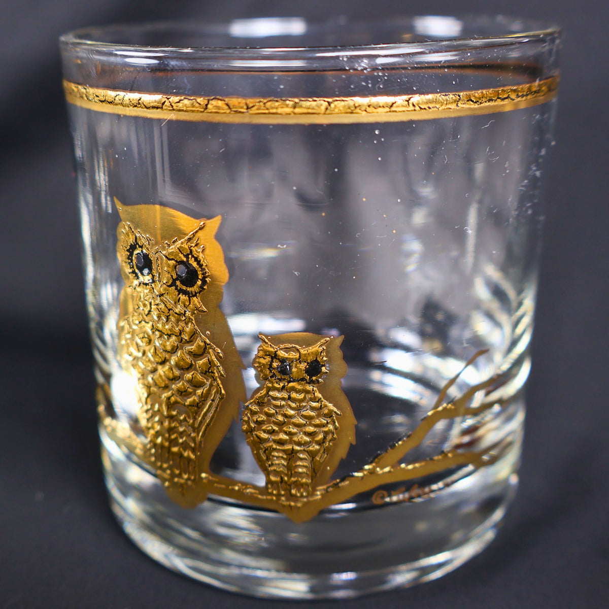 Close front view of one vintage Culver owl rocks glass showing a large and small owl in raised gold decoration on a branching perch. The clear lowball glass has a narrow gold rim and visible vintage surface character beneath the detailed bird motif.