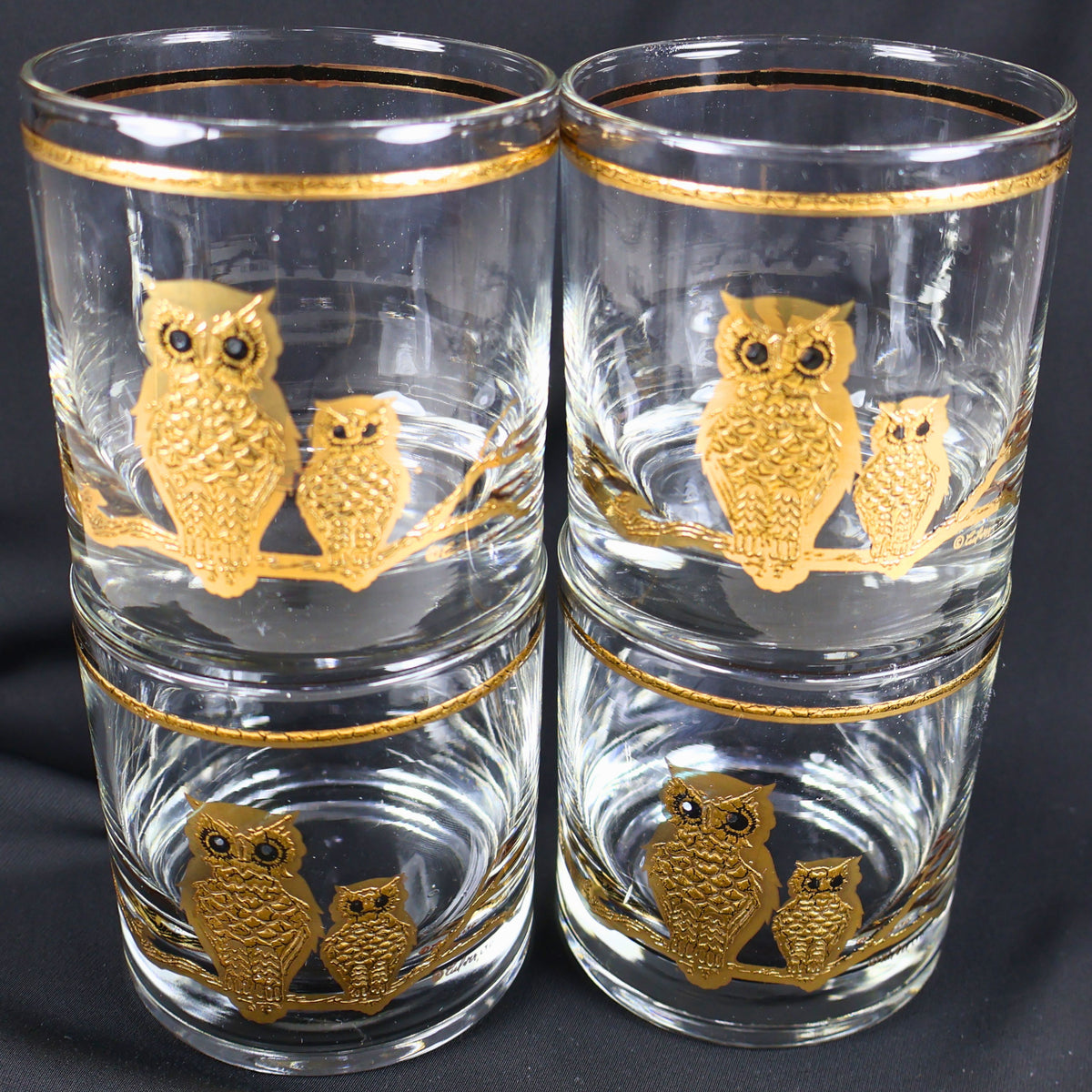 Four Culver owl lowball glasses arranged in a compact stacked display. The front-facing pair of clear tumblers shows textured gold adult and smaller owls perched together, with matching gold rim bands creating a cohesive mid-century barware set.