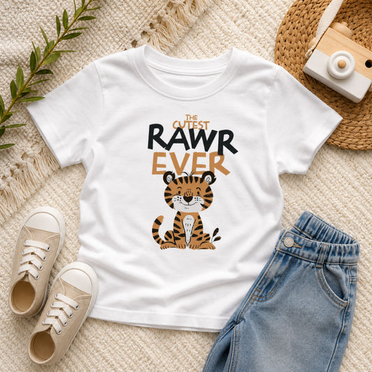 Cute tiger toddler tee with “Cutest RAWR Ever” graphic printed on a white Bella Canvas shirt, styled in a neutral flat lay with denim jeans and soft textures for a modern boutique kids outfit look.
