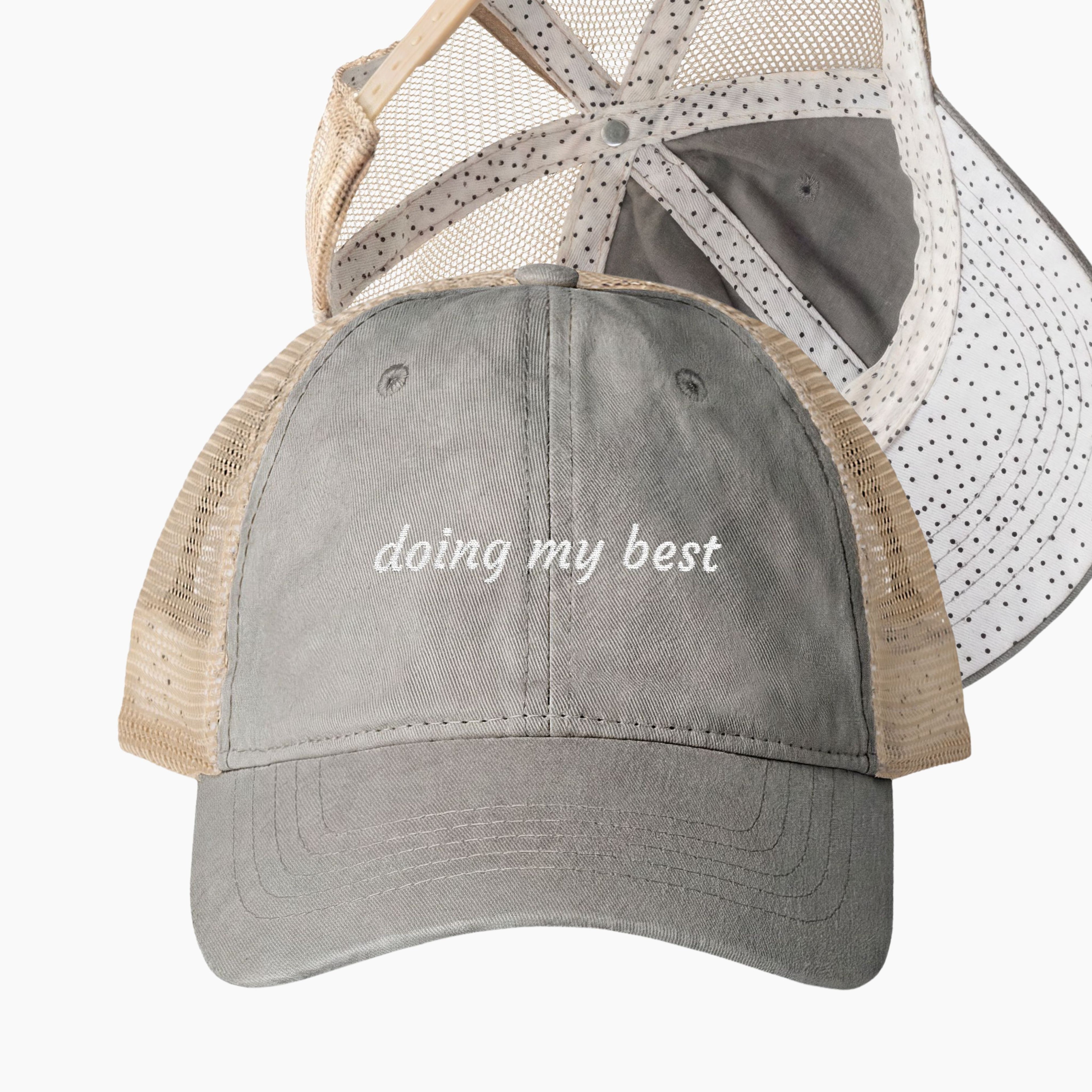 Gray and tan mesh back trucker hat with doing my best embroidered saying and black polka dot patterned underrim