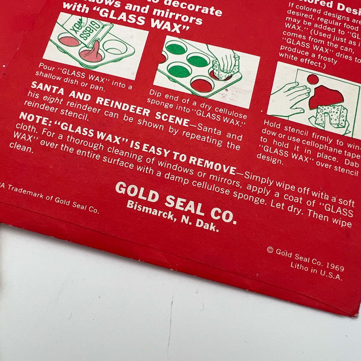 Close-up of the red Christmas stencil package showing illustrated Glass Wax application instructions, the Gold Seal Company Bismarck address, and a 1969 copyright beside the Litho in U.S.A. marking. Creasing and small areas of wear appear along the bottom edge.