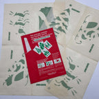 Four vintage Glass Wax Christmas stencil sheets arranged beneath their red Gold Seal envelope. Reindeer, Christmas tree, angel, and Santa sleigh motifs appear across cream paper with green printing and visible folds; the envelope shows instructions and paper loss.