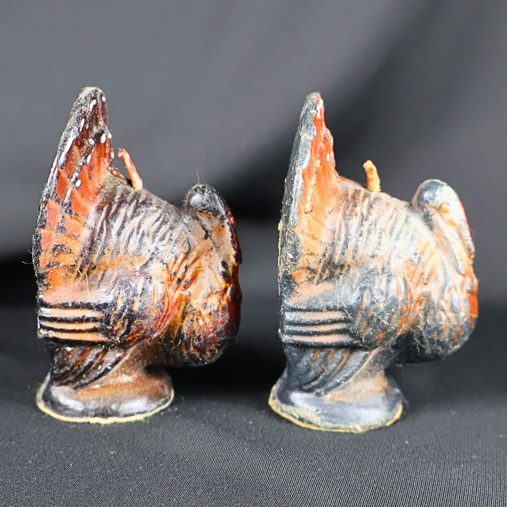 Side profiles of two small vintage Gurley Thanksgiving turkey candles. The photograph shows their dimensional molded wings, layered feather patterns, fan-shaped tails, projecting wicks and dark pedestal bases, along with worn orange, brown and black surface coloring.