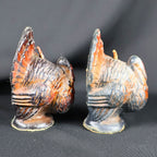 Side profiles of two small vintage Gurley Thanksgiving turkey candles. The photograph shows their dimensional molded wings, layered feather patterns, fan-shaped tails, projecting wicks and dark pedestal bases, along with worn orange, brown and black surface coloring.