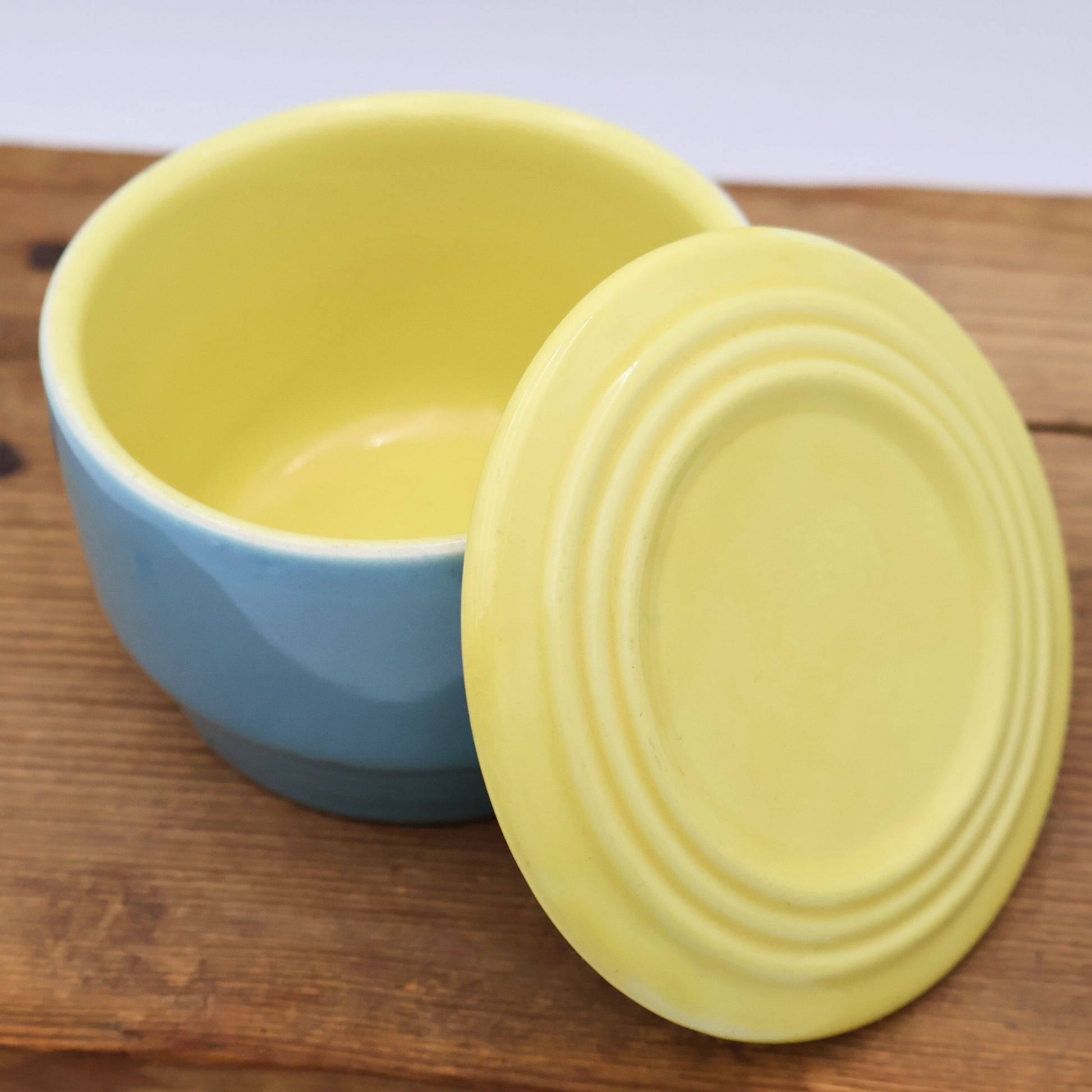 Hall China refrigerator dish with lid removed showing glossy butter yellow interior and blue exterior, mid century kitchen storage.