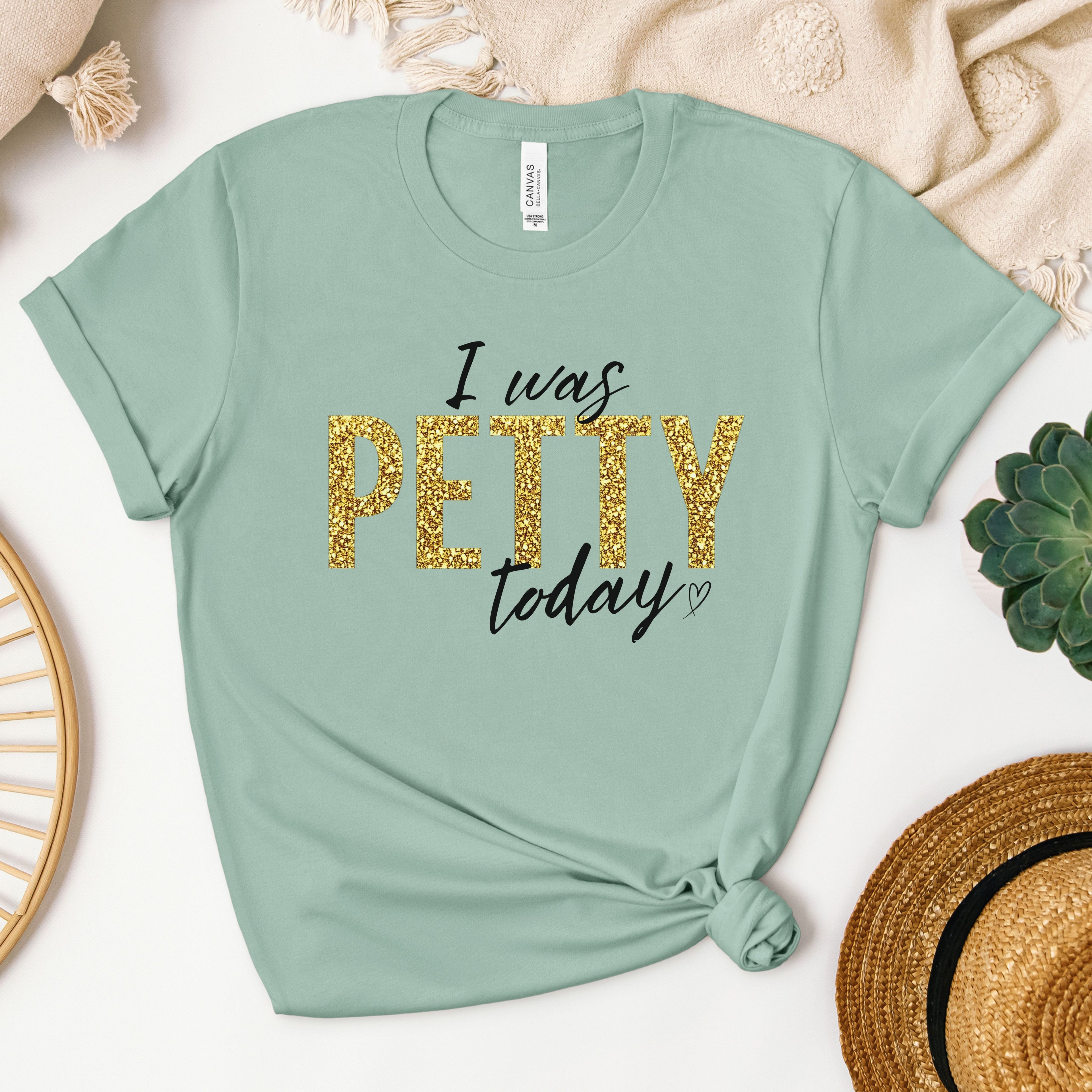 Sage green t-shirt with gold faux glitter “I Was Petty Today” graphic, soft muted tone flat lay, trendy women’s statement tee, funny sarcastic boutique apparel