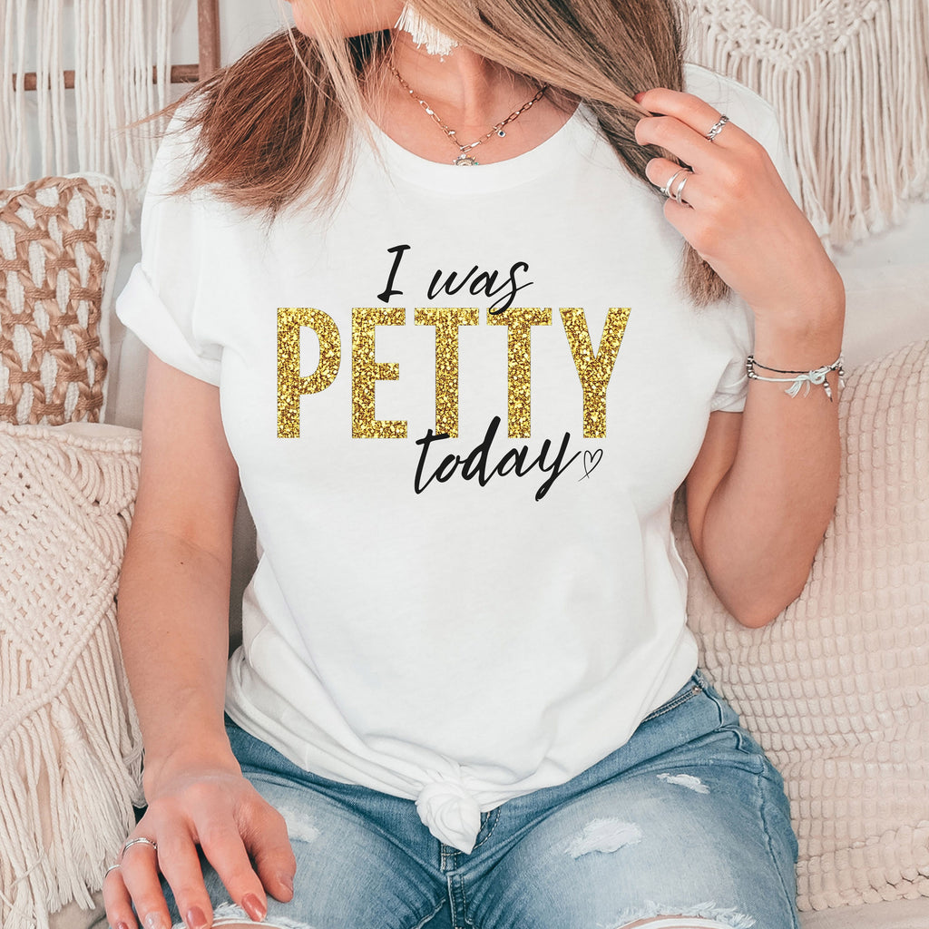 Woman wearing white “I Was Petty Today” gold faux glitter graphic t-shirt, relaxed casual outfit, cute sarcastic statement tee for women, soft comfortable everyday style