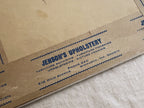 Close-up of blue Jenson’s Upholstery printing on brown framing tape. The label lists furniture repairing, furniture finishing, upholstering, picture framing, Phone 240, and 510 Main Avenue in Bismarck, North Dakota, with backing discoloration visible above.