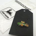 John Deere tractor enamel lapel pin displayed on original backing card with branded packaging, featuring green and yellow farm tractor design with gold tone metal, collectible farming pin for hats, jackets, or rural western style outfits