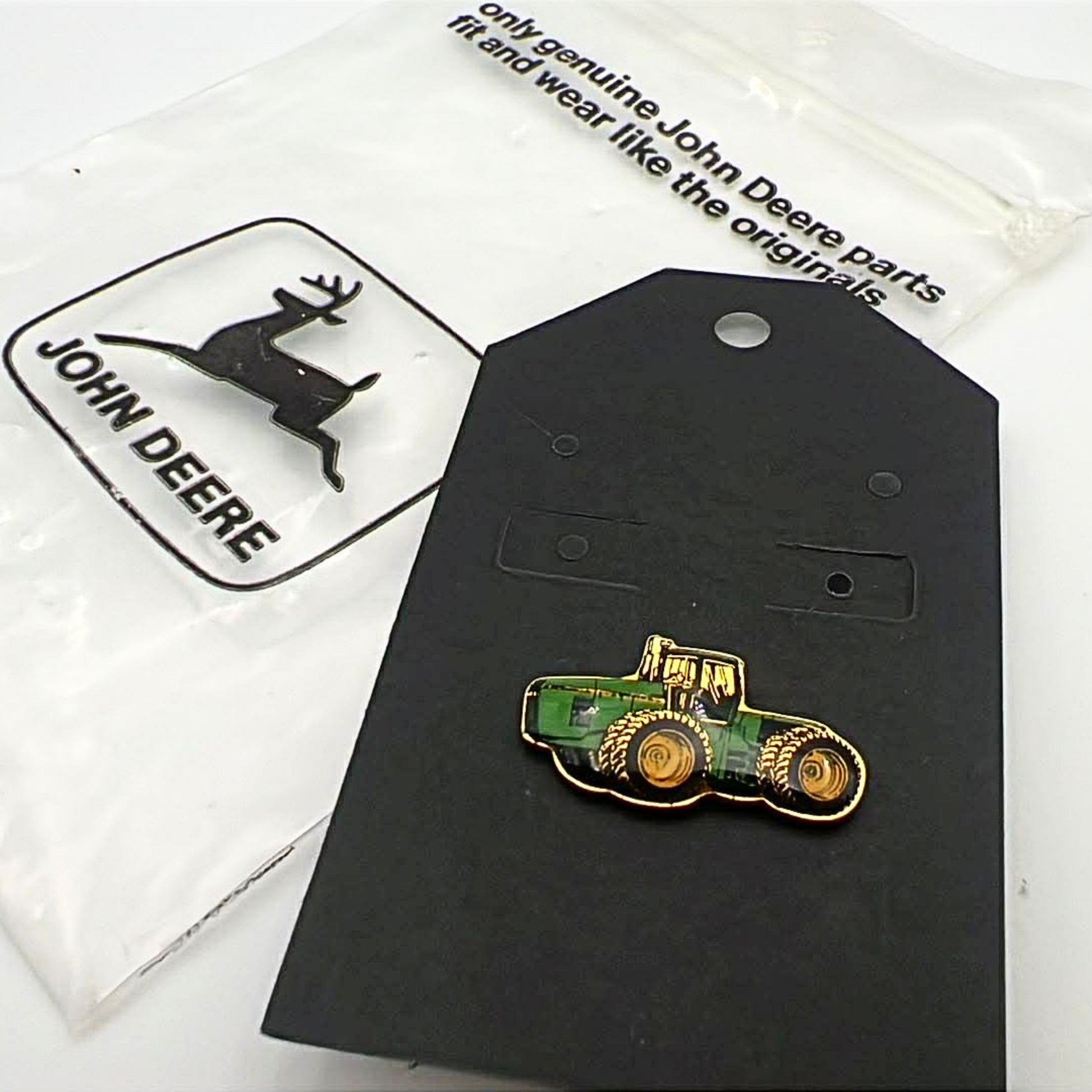 John Deere tractor enamel lapel pin displayed on original backing card with branded packaging, featuring green and yellow farm tractor design with gold tone metal, collectible farming pin for hats, jackets, or rural western style outfits